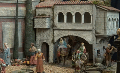 Detalle de un Belén tradicional que muestra figuras detalladas de los Reyes Magos a caballo en el centro, aproximándose a una edificación de estilo antiguo.