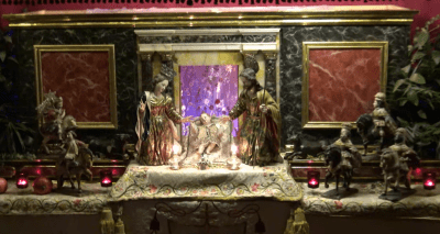 Figuras de la Natividad con la Sagrada Familia y el Niño Jesús en el centro, flanqueados por los Reyes Magos a caballo en un Belén ricamente decorado.