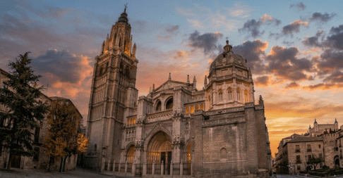 Vista panorámica de la Catedral de Toledo bajo un cielo de atardecer con nubes suaves y tonos anaranjados que iluminan la fachada gótica y su gran torre.